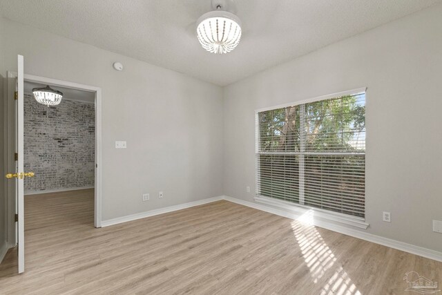 spare room with light hardwood / wood-style flooring, a chandelier, and a textured ceiling