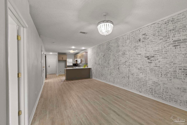 unfurnished living room featuring a chandelier, a textured ceiling, and light wood-type flooring