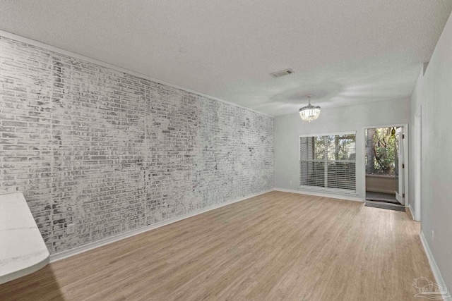 empty room with a chandelier, light hardwood / wood-style floors, and a textured ceiling