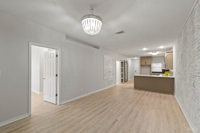 unfurnished living room featuring a chandelier, a textured ceiling, and light hardwood / wood-style floors