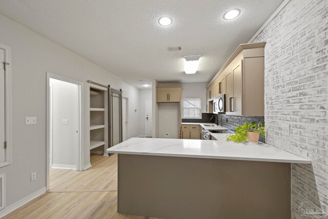 kitchen with stainless steel appliances, a barn door, light hardwood / wood-style flooring, kitchen peninsula, and a textured ceiling