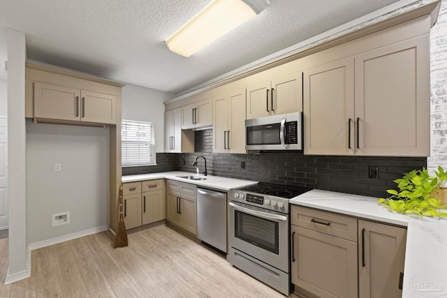 kitchen featuring sink, stainless steel appliances, tasteful backsplash, light hardwood / wood-style floors, and a textured ceiling