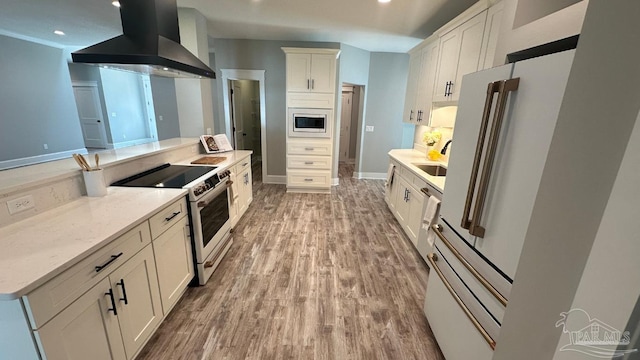 kitchen featuring wall chimney range hood, white cabinets, light wood-type flooring, light stone counters, and high end appliances