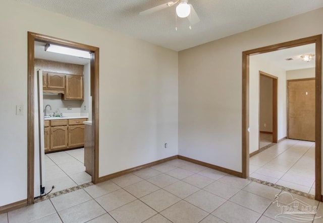 spare room with light tile patterned floors, ceiling fan, a textured ceiling, and baseboards