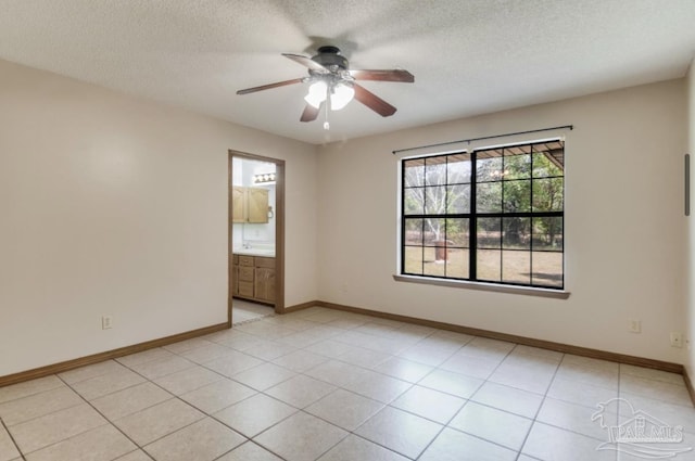 empty room featuring a textured ceiling, light tile patterned flooring, a ceiling fan, and baseboards