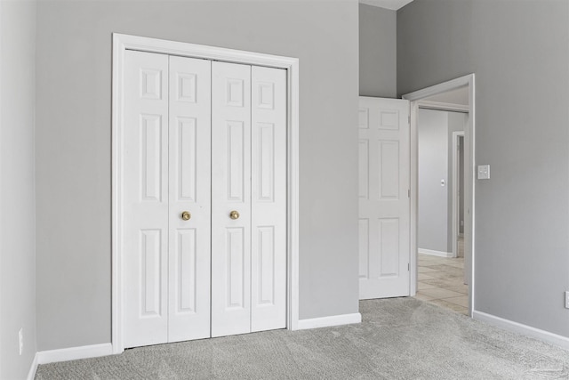 unfurnished bedroom with a closet, light carpet, and baseboards