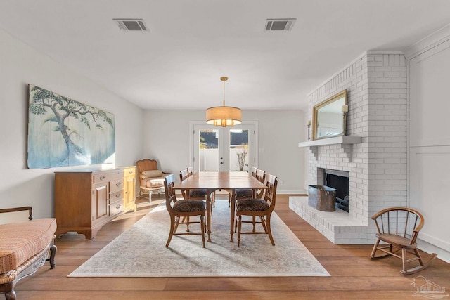 dining area featuring a brick fireplace, light hardwood / wood-style flooring, and french doors