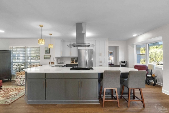 kitchen featuring sink, stainless steel refrigerator, hanging light fixtures, white cabinets, and island range hood