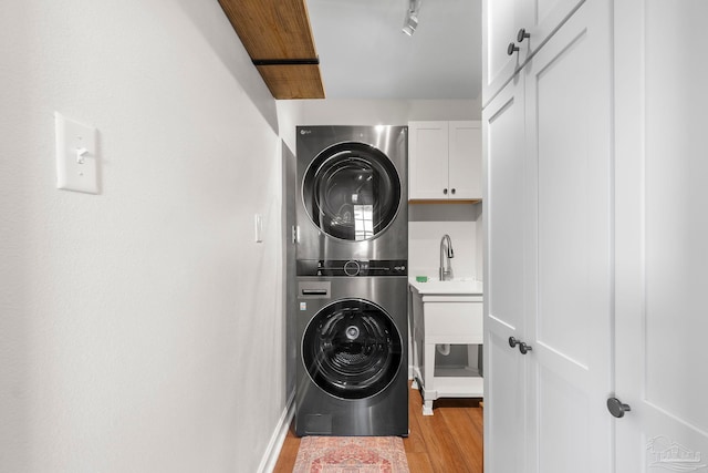 laundry room featuring stacked washer / dryer, light hardwood / wood-style floors, and cabinets