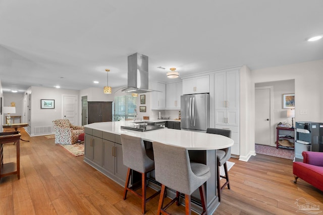 kitchen featuring pendant lighting, island exhaust hood, stainless steel refrigerator, white cabinetry, and light wood-type flooring