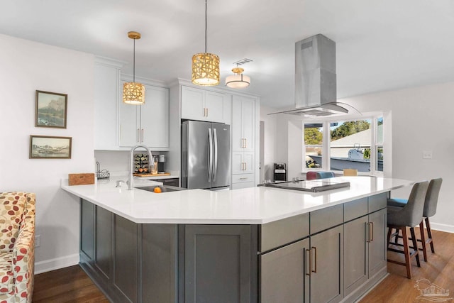 kitchen featuring kitchen peninsula, sink, island exhaust hood, stainless steel refrigerator, and hanging light fixtures