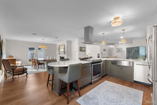 kitchen featuring kitchen peninsula, island exhaust hood, appliances with stainless steel finishes, hanging light fixtures, and sink