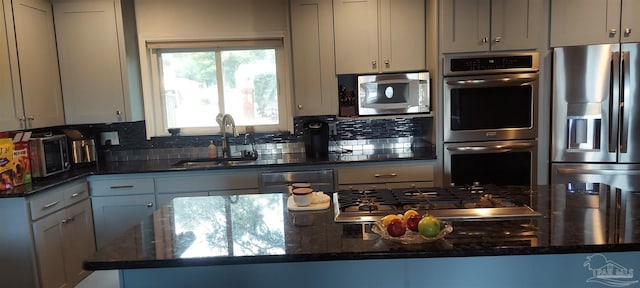 kitchen featuring appliances with stainless steel finishes, sink, gray cabinetry, backsplash, and dark stone counters