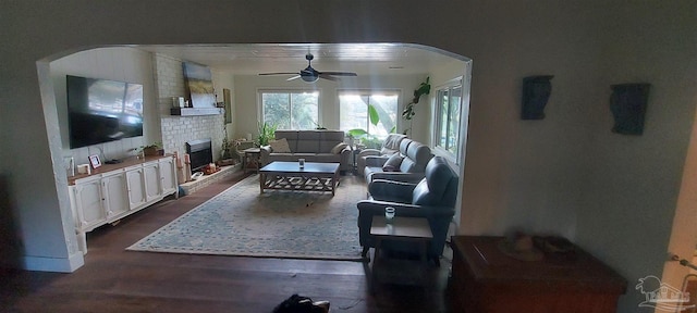 living room featuring ceiling fan, a brick fireplace, and dark hardwood / wood-style flooring