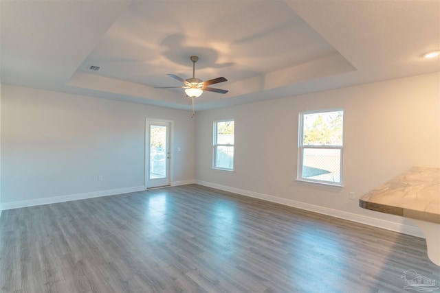 unfurnished room with a raised ceiling, ceiling fan, and dark wood-type flooring