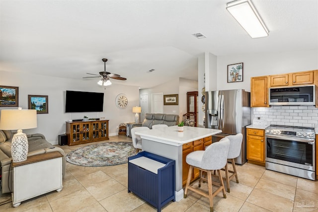 kitchen featuring appliances with stainless steel finishes, ceiling fan, a breakfast bar area, a kitchen island, and lofted ceiling