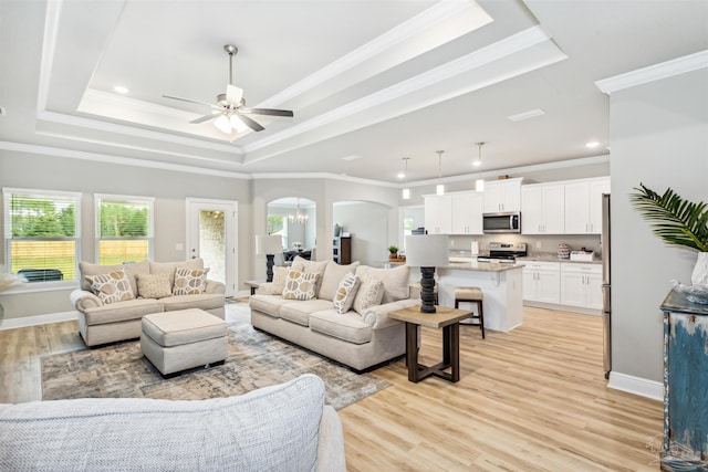 living room with ceiling fan, light hardwood / wood-style floors, ornamental molding, and a tray ceiling