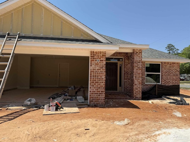 view of front of house featuring brick siding, a shingled roof, and board and batten siding