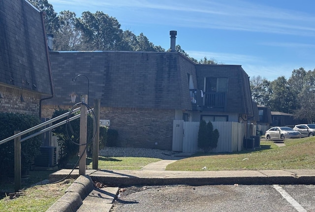 view of side of home with mansard roof, a lawn, roof with shingles, cooling unit, and brick siding