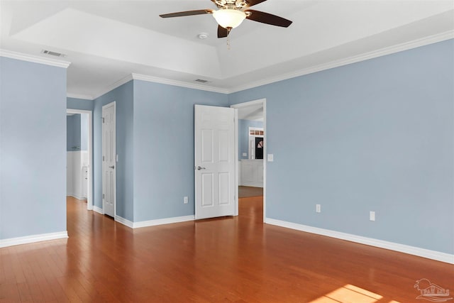 empty room with a tray ceiling, ceiling fan, ornamental molding, and hardwood / wood-style flooring