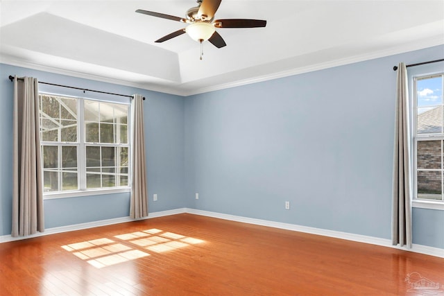 empty room featuring a raised ceiling, ceiling fan, hardwood / wood-style floors, and ornamental molding