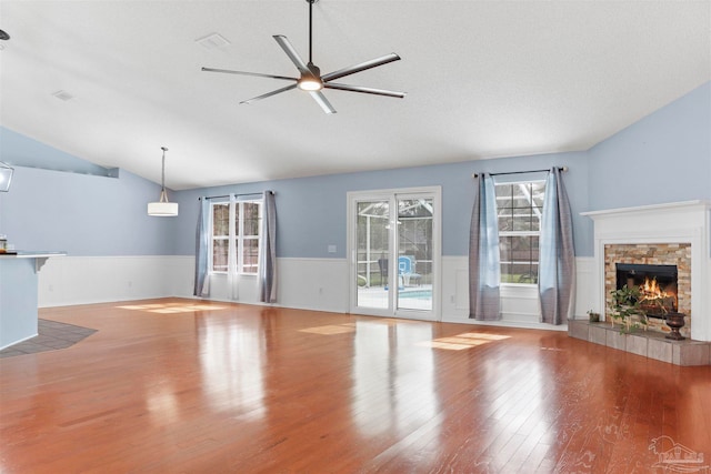 unfurnished living room with ceiling fan, a stone fireplace, a textured ceiling, vaulted ceiling, and light wood-type flooring