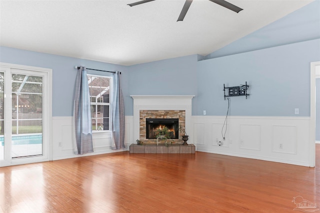 unfurnished living room with a stone fireplace, ceiling fan, lofted ceiling, and hardwood / wood-style flooring