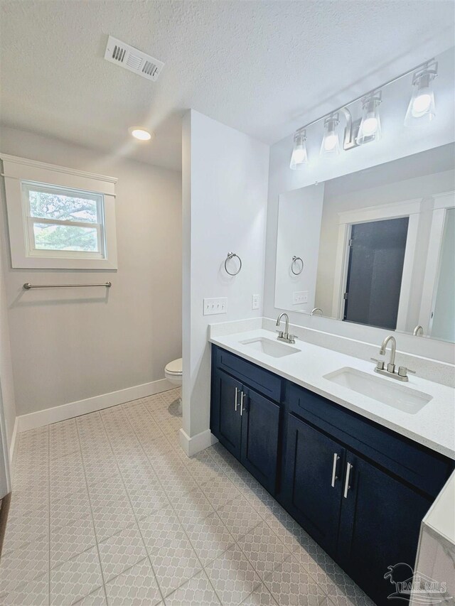 bathroom with double vanity, tile patterned flooring, toilet, and a textured ceiling