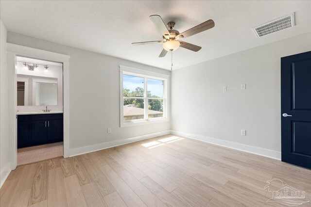 unfurnished bedroom with ceiling fan, ensuite bath, light wood-type flooring, sink, and a textured ceiling