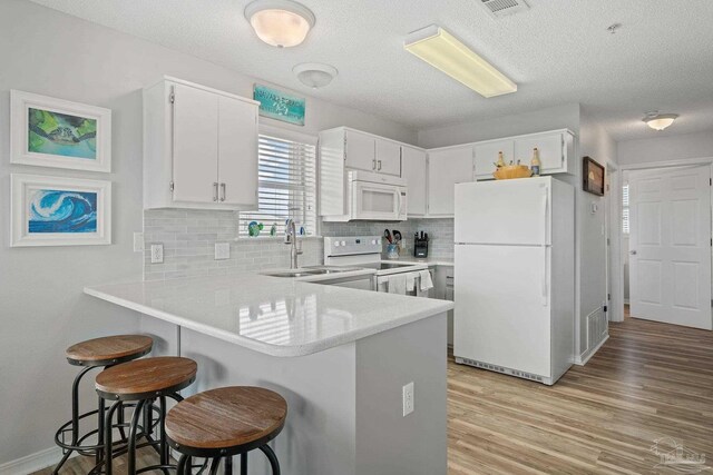 7464 Sunset Harbor Dr Unit 133, Navarre Beach, FL 32566 - kitchen featuring white cabinetry, white appliances, kitchen peninsula, and a kitchen bar