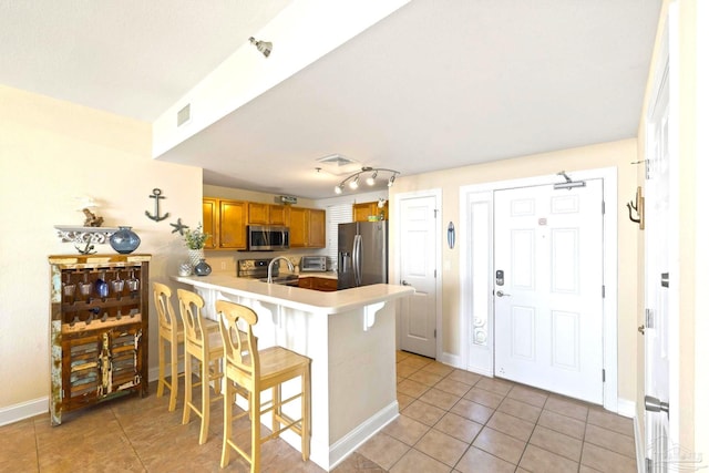 kitchen featuring a breakfast bar, kitchen peninsula, light tile patterned flooring, sink, and appliances with stainless steel finishes