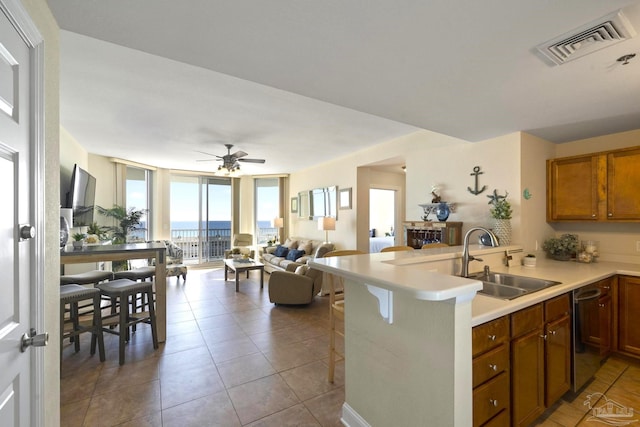 kitchen featuring dishwasher, sink, light tile patterned flooring, expansive windows, and a breakfast bar area