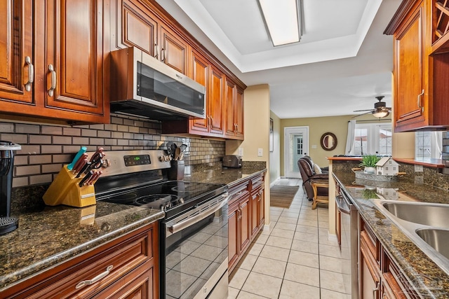 kitchen featuring light tile patterned floors, ceiling fan, appliances with stainless steel finishes, backsplash, and dark stone counters