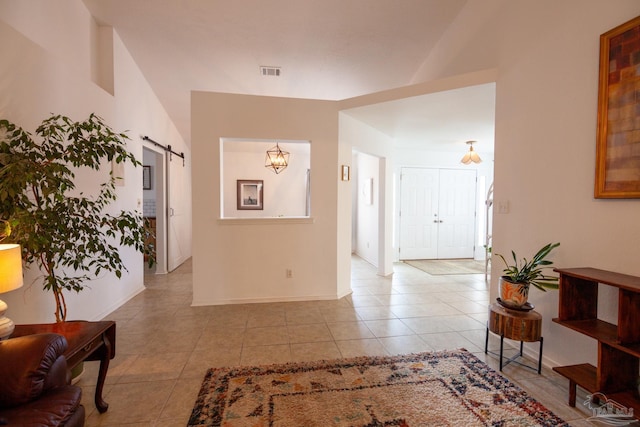 hallway featuring light tile patterned floors, a barn door, visible vents, and baseboards