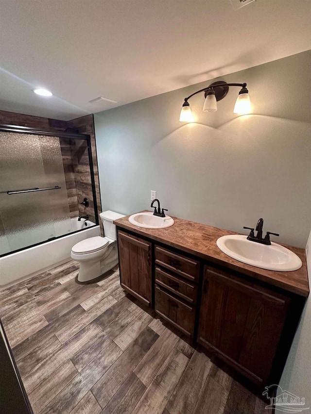 full bathroom with shower / bath combination with glass door, hardwood / wood-style floors, vanity, and toilet