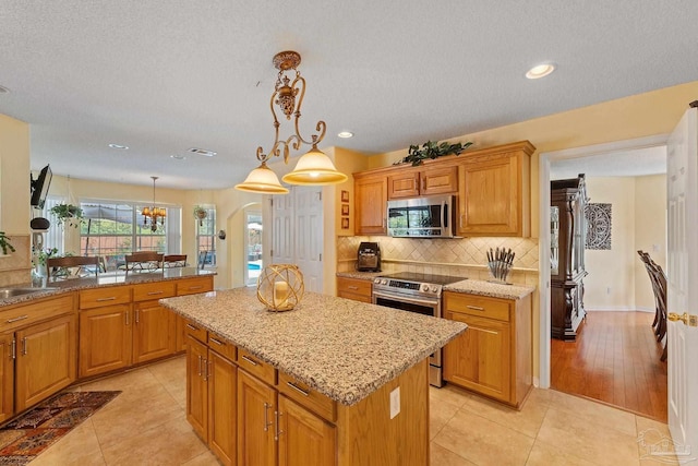 kitchen with a kitchen island, stainless steel appliances, decorative light fixtures, and light tile patterned floors