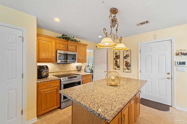 kitchen featuring appliances with stainless steel finishes, backsplash, light stone countertops, a kitchen island, and light tile patterned flooring