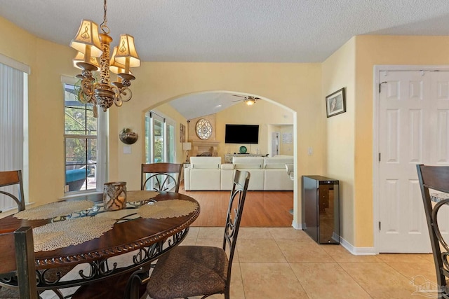 dining space with light wood-type flooring, a chandelier, beverage cooler, vaulted ceiling, and a textured ceiling