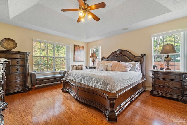 bedroom with a tray ceiling, ceiling fan, a textured ceiling, and hardwood / wood-style flooring