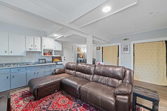 living room featuring beam ceiling, sink, crown molding, hardwood / wood-style floors, and a textured ceiling