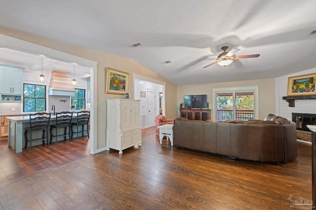 living room with a fireplace, vaulted ceiling, ceiling fan, and dark wood-type flooring