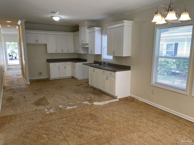 kitchen with sink, white cabinetry, a textured ceiling, ornamental molding, and pendant lighting