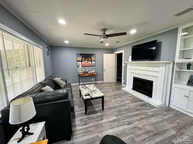 living room featuring ceiling fan, hardwood / wood-style flooring, a fireplace, and a textured ceiling