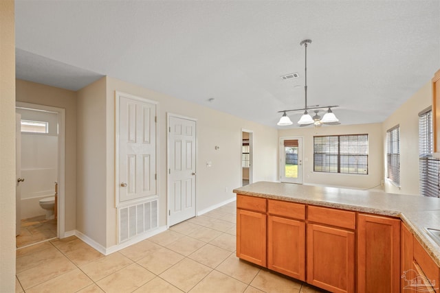 kitchen with light tile patterned floors, visible vents, brown cabinets, decorative light fixtures, and light countertops