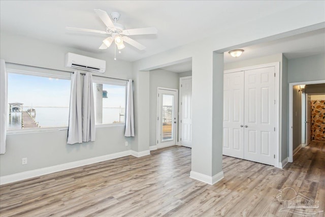 unfurnished bedroom featuring a wall mounted air conditioner, ceiling fan, and light hardwood / wood-style flooring