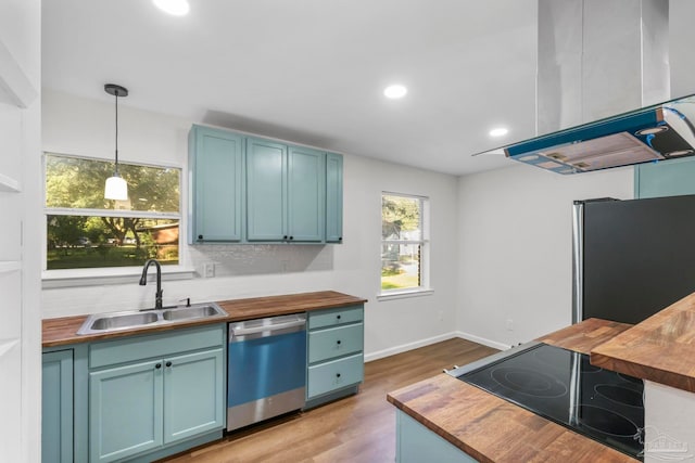 kitchen with pendant lighting, sink, range hood, appliances with stainless steel finishes, and butcher block counters