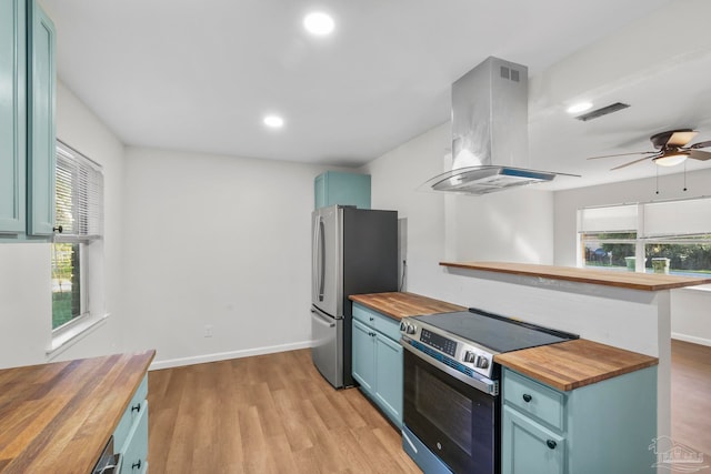 kitchen featuring wood counters, plenty of natural light, wall chimney range hood, and stainless steel appliances