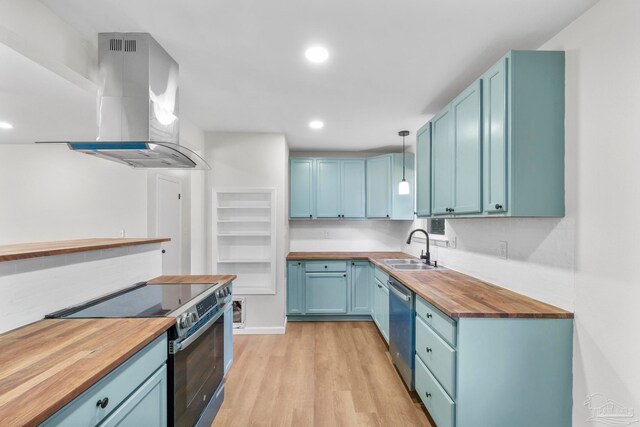 kitchen featuring sink, butcher block countertops, decorative light fixtures, stainless steel appliances, and extractor fan