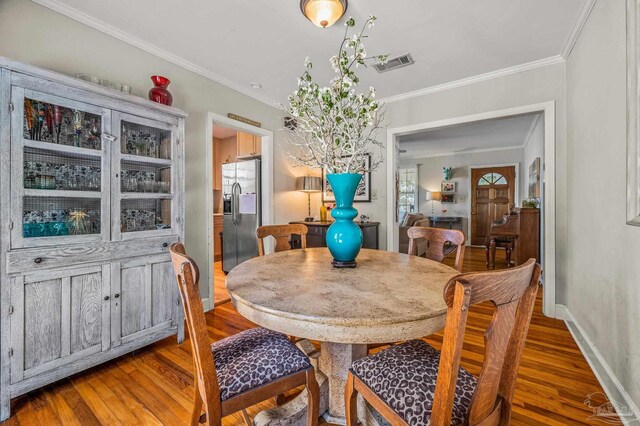 dining room with baseboards, visible vents, crown molding, and wood finished floors
