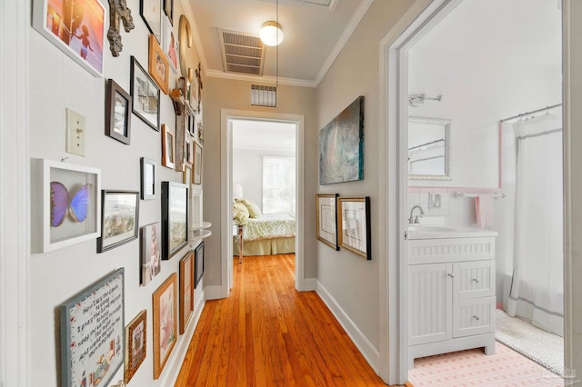 corridor with light wood finished floors, visible vents, ornamental molding, and a sink